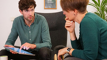 Man i grön skjorta samtalar med kvinna och pekar på en digital platta